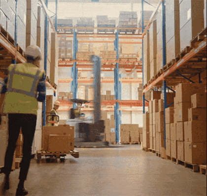 Forklift lifting pallets between high warehouse racks while staff pick boxes